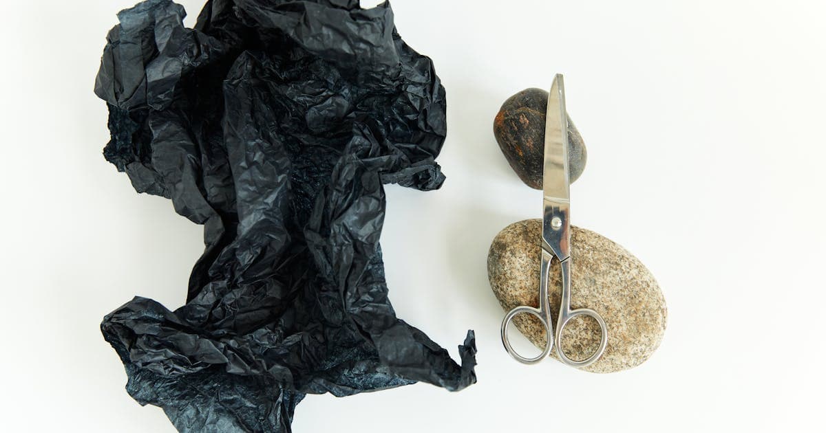 Silver scissors beside crumpled black paper on white background, a creative take on the classic game elements