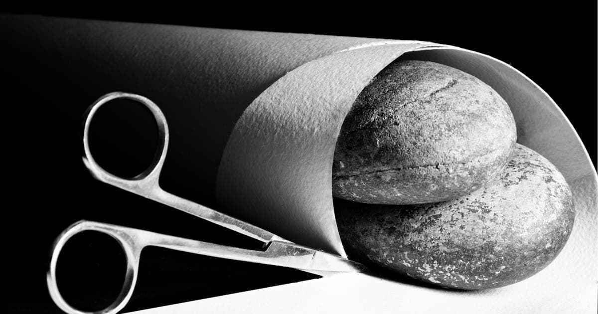 Monochrome still life of rocks wrapped in paper with scissors representing the game elements